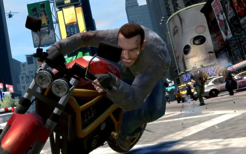 Niko Bellic penché à fond sur une moto sportive rouge en pleine course à Star Junction, le carrefour à néons de Liberty City, hélicoptère dans le ciel et voitures de police à droite