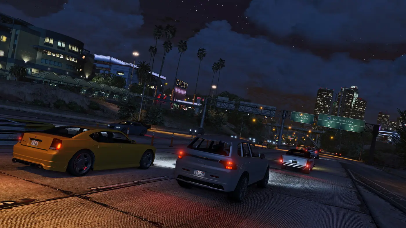 Capture de GTA 5 : circulation nocturne sur l'autoroute de Los Santos, palmiers, néons d'un casino et gratte-ciels du centre-ville en arrière-plan