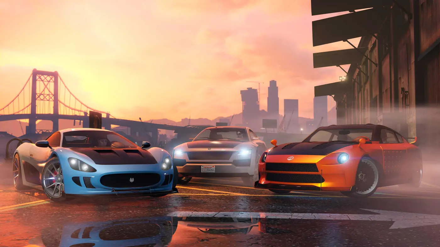 Capture officielle GTA Online : trois sportives, une supercar bleue, une berline blanche aux phares allumés et un coupé tuné orange, alignées sur une route mouillée au coucher du soleil, avec un pont et la skyline de Los Santos en arrière-plan