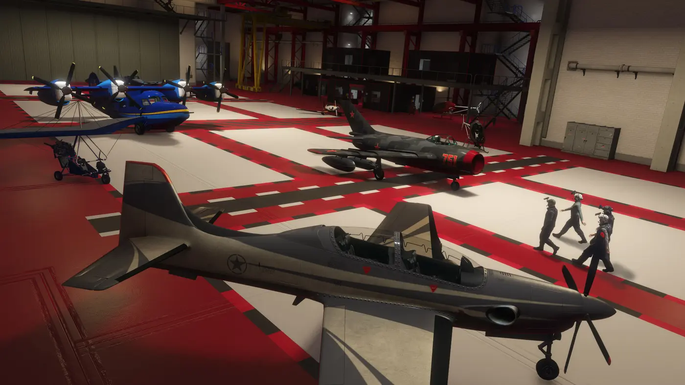 Un hangar personnel de GTA Online rempli d'aéronefs : un hydravion bleu, un chasseur camouflé numéro 751, un petit hélicoptère, un ultraléger et un avion-école gris, avec des pilotes en combinaison qui traversent la piste