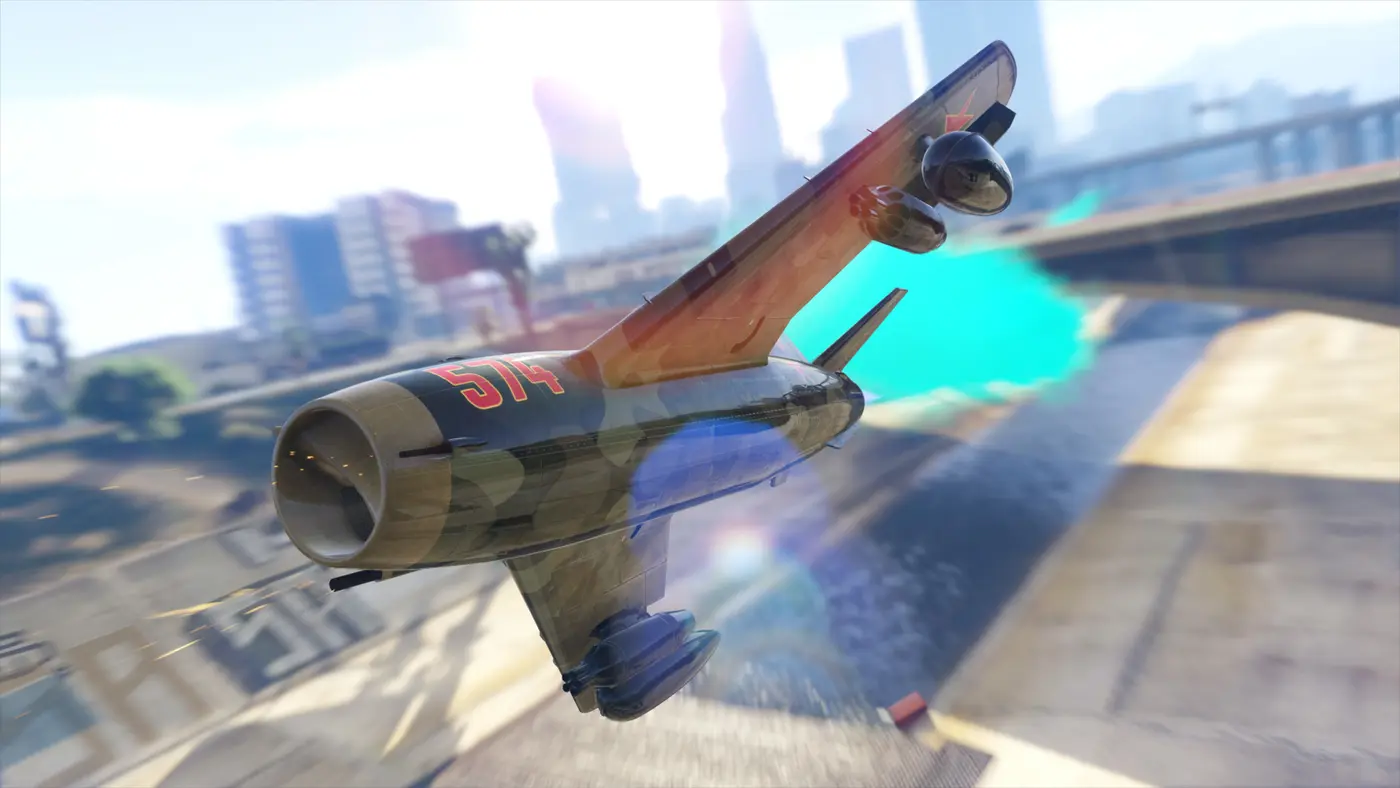 Un jet de chasse camouflé numéro 574 file au ras de l'aqueduc de Los Santos dans GTA Online, postcombustion allumée, gratte-ciel du centre-ville en arrière-plan
