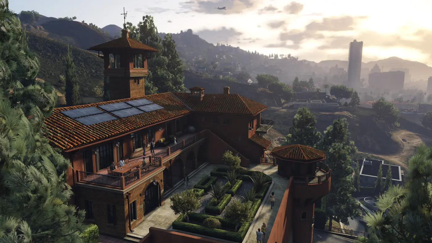 Vue aérienne d'un manoir de Vinewood Hills entouré de collines, surplombant la skyline de Los Santos dans une lumière de coucher de soleil