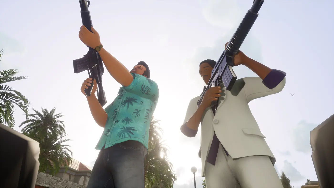 Deux membres du gang Vercetti, dont Tommy en chemise hawaïenne turquoise, brandissent des fusils d'assaut M4 vers le ciel dans une rue de Vice City ensoleillée bordée de palmiers, dans le remaster Definitive Edition