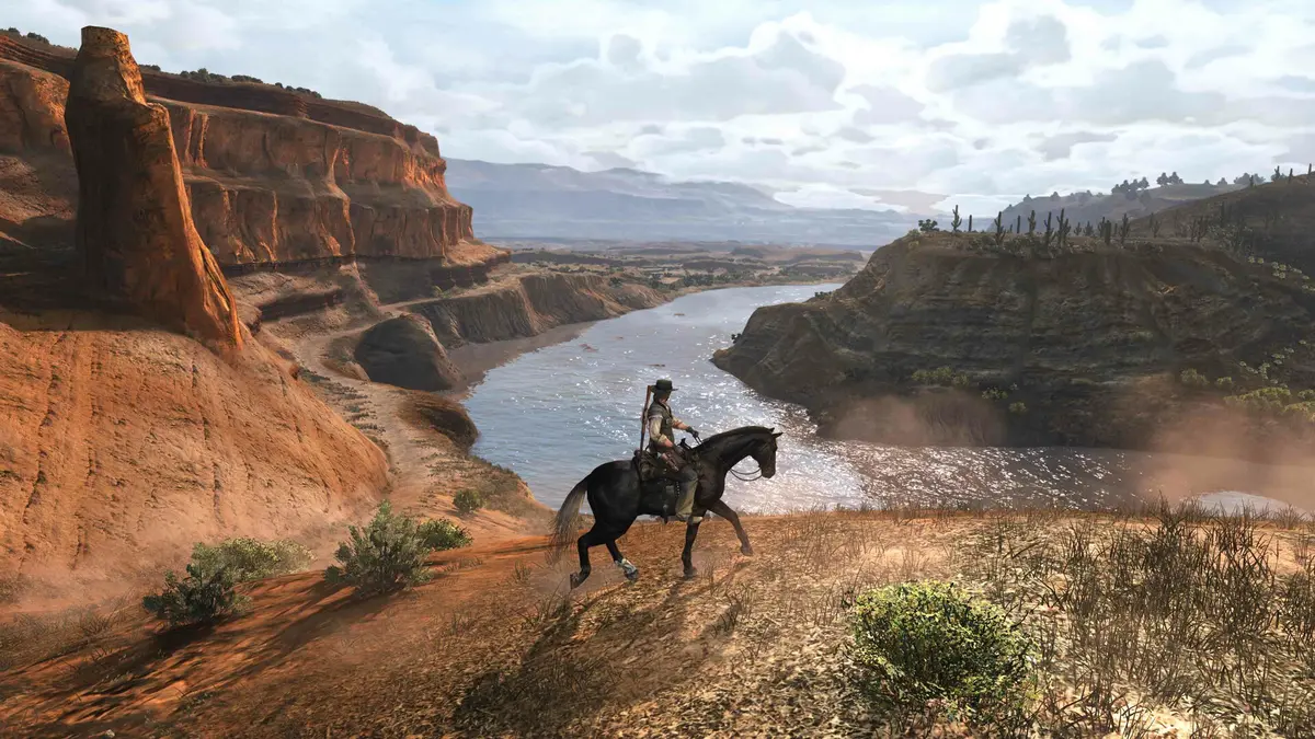 Un cavalier sur un cheval noir longe le bord d'un canyon de roche rouge au-dessus d'une rivière, sous un ciel nuageux
