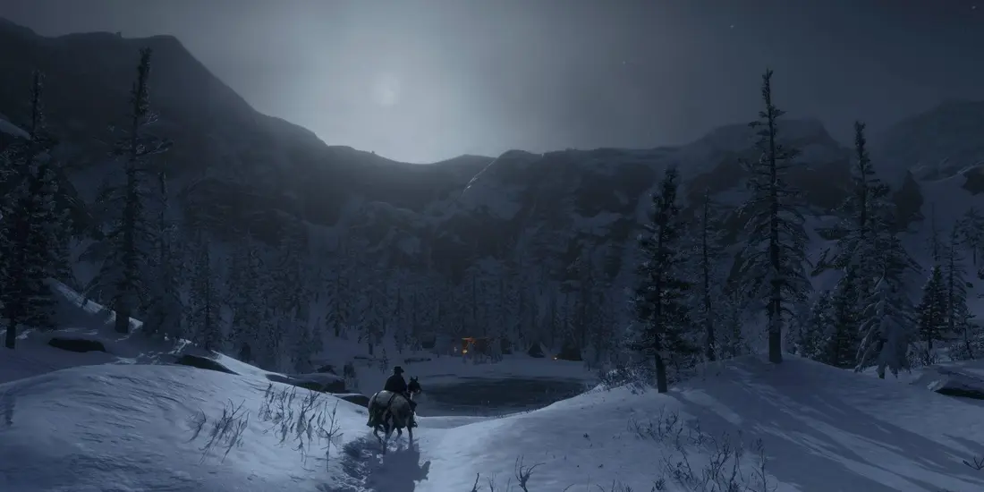 Cavalier solitaire chevauchant dans un paysage de montagnes enneigées la nuit, sous une lune voilée, vers un lac gelé bordé de sapins dans Red Dead Redemption 2