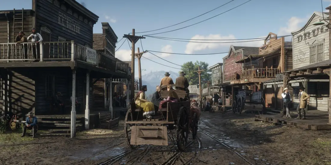 Rue principale boueuse d'une ville de l'Ouest dans Red Dead Redemption 2 : façades en bois d'une armurerie et d'un drugstore, passants, calèche tirée par un cheval et montagnes au fond