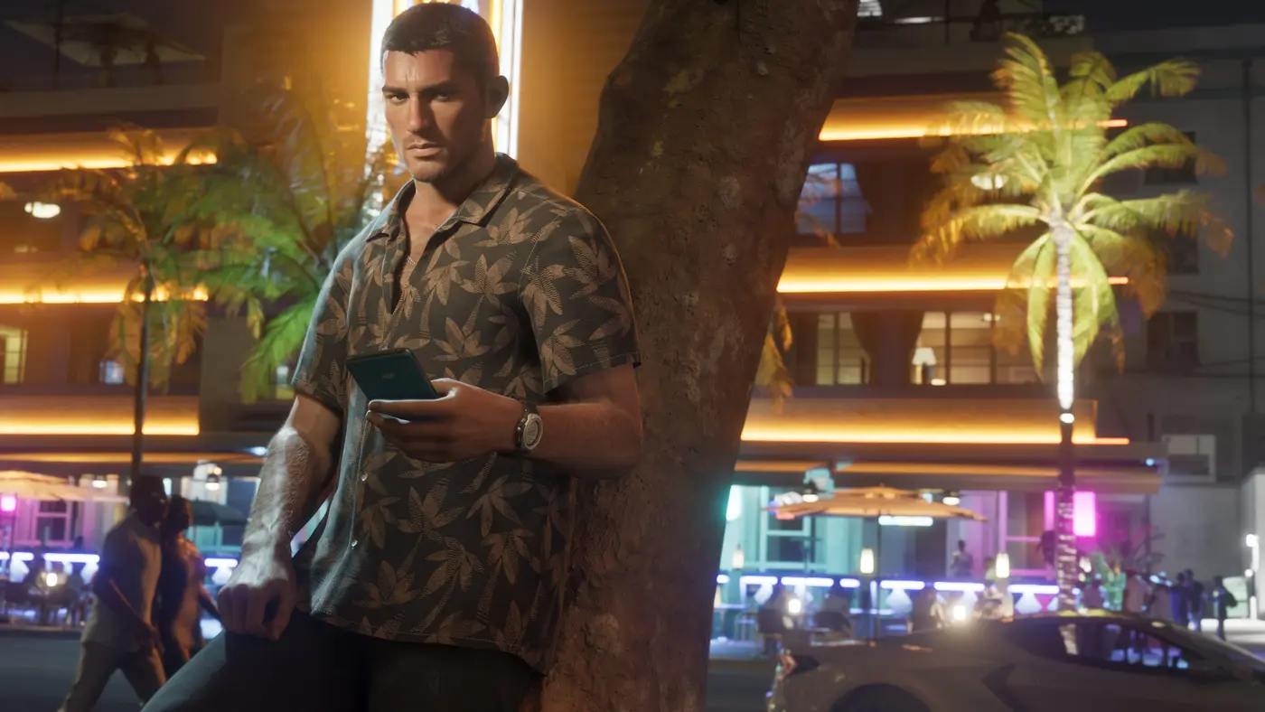 Jason Duval de nuit à Vice City, en chemise à motif végétal, un téléphone à la main, adossé à un arbre devant un immeuble aux néons dorés bordé de palmiers