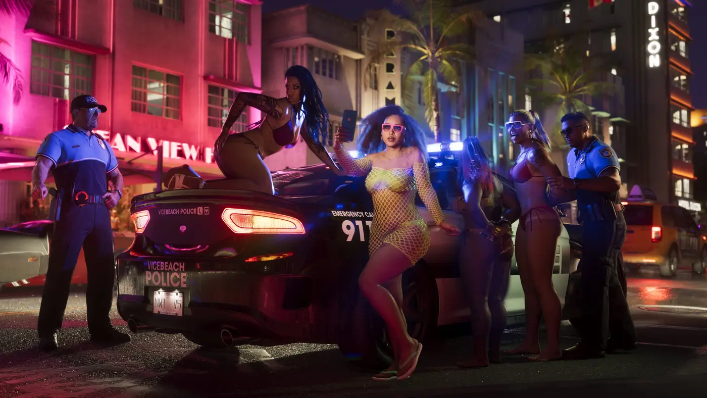 Rue de Vice City la nuit dans GTA VI, un groupe de jeunes femmes dont une prend un selfie au smartphone devant une voiture de police noire marquée VICEBEACH POLICE et EMERGENCY CALL 911, deux agents et des hôtels Art déco au néon rose
